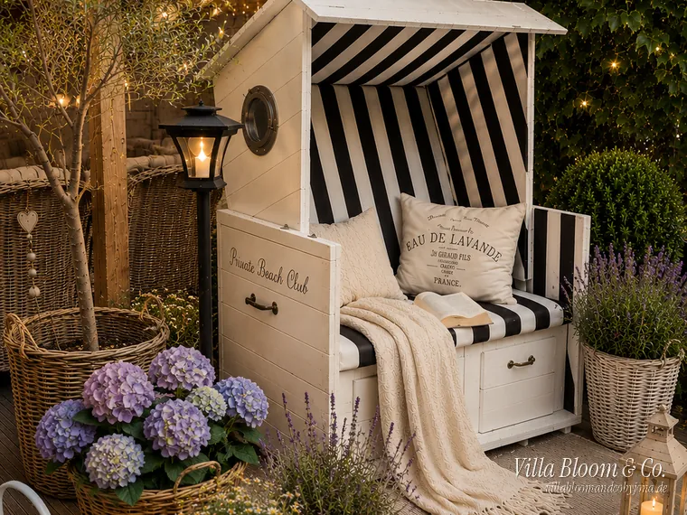 Gemütliche Sommerterrasse im Landhausstil mit Strandkorb, Hortensien, Lavendel und Lichterketten am Abend