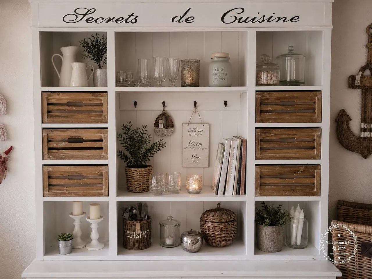 Offenes Landhaus-Regal mit Secrets de Cuisine Schriftzug, Holzkisten, weißen Krügen, Gläsern und Körben im Riviera-Maison-Stil
