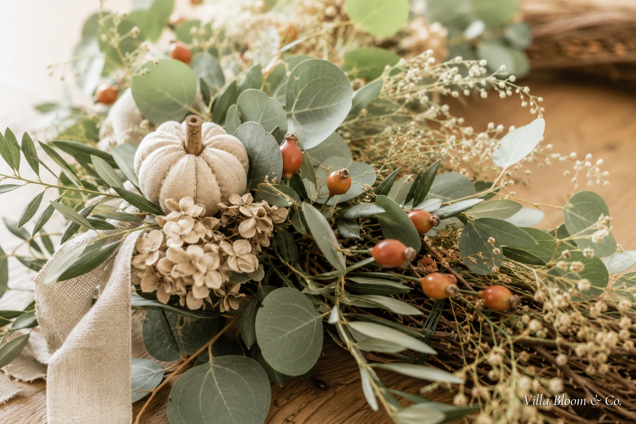 Fertig gebundener Herbstkranz aus Eukalyptus und Trockenblumen auf dem Esstisch, daneben Band und Schere