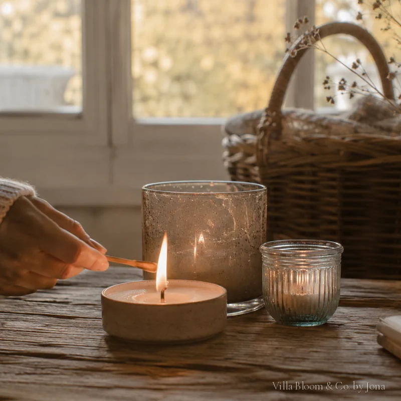Lighting a candle with a match, a basket and dried flowers nearby