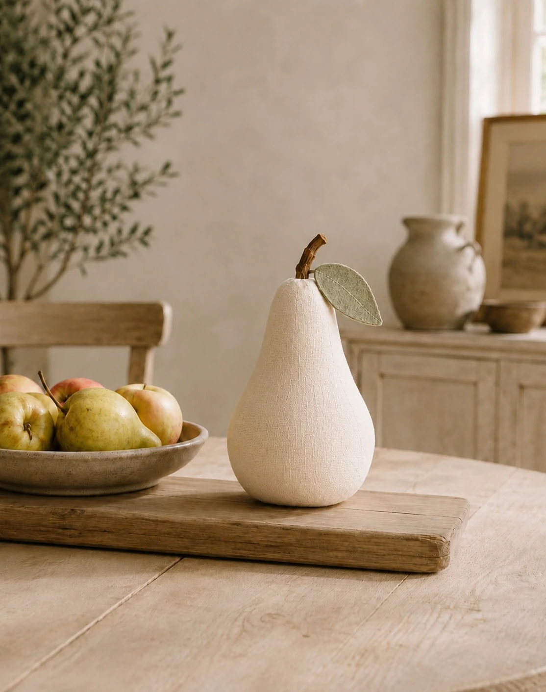 Einzelne Leinenbirne auf einem Holztisch im hellen Landhaus-Wohnzimmer, dahinter Sessel, Sideboard und Vase