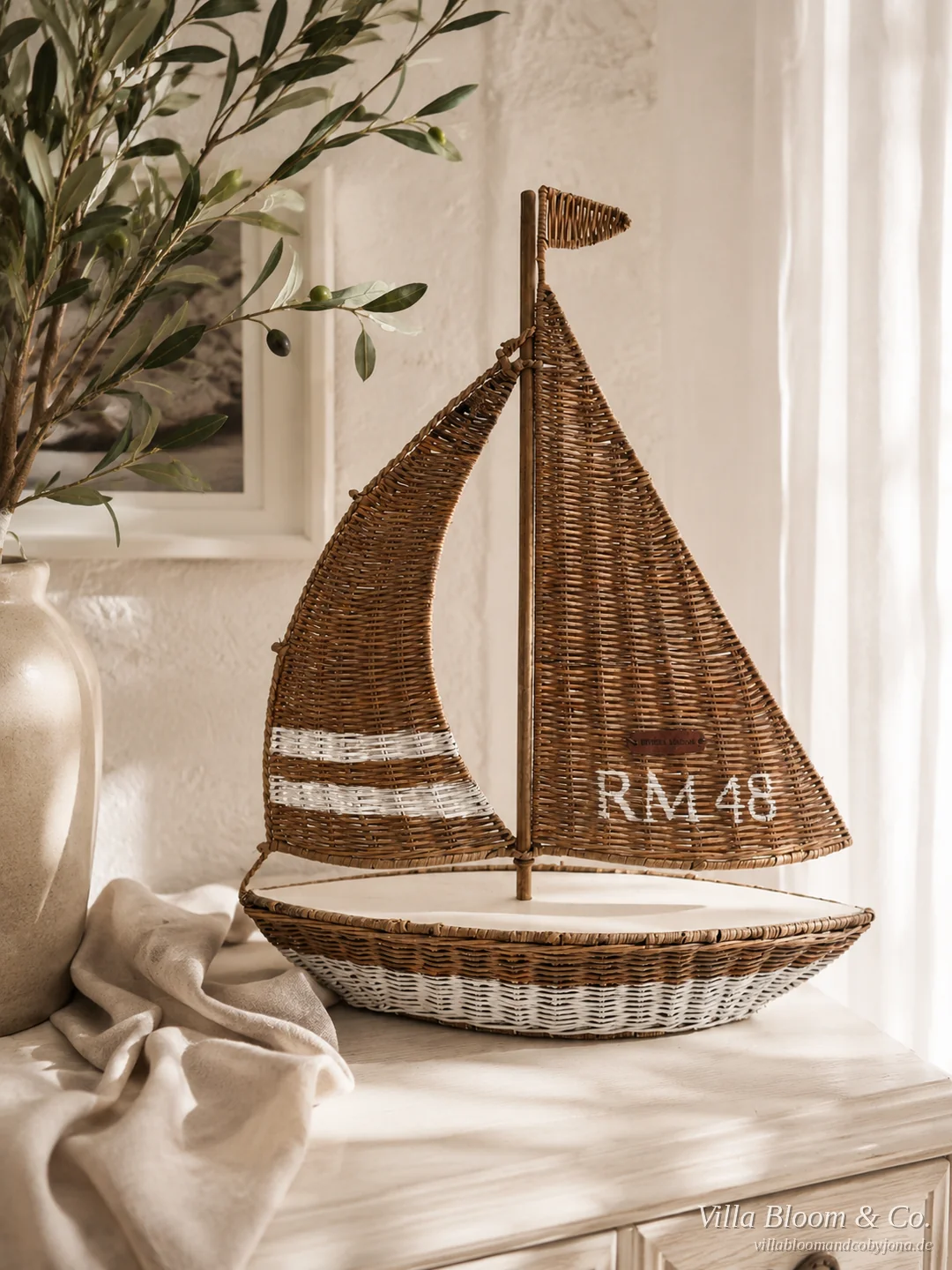 Segelboot aus Rattan mit der Aufschrift RM 48 neben einem Olivenzweig