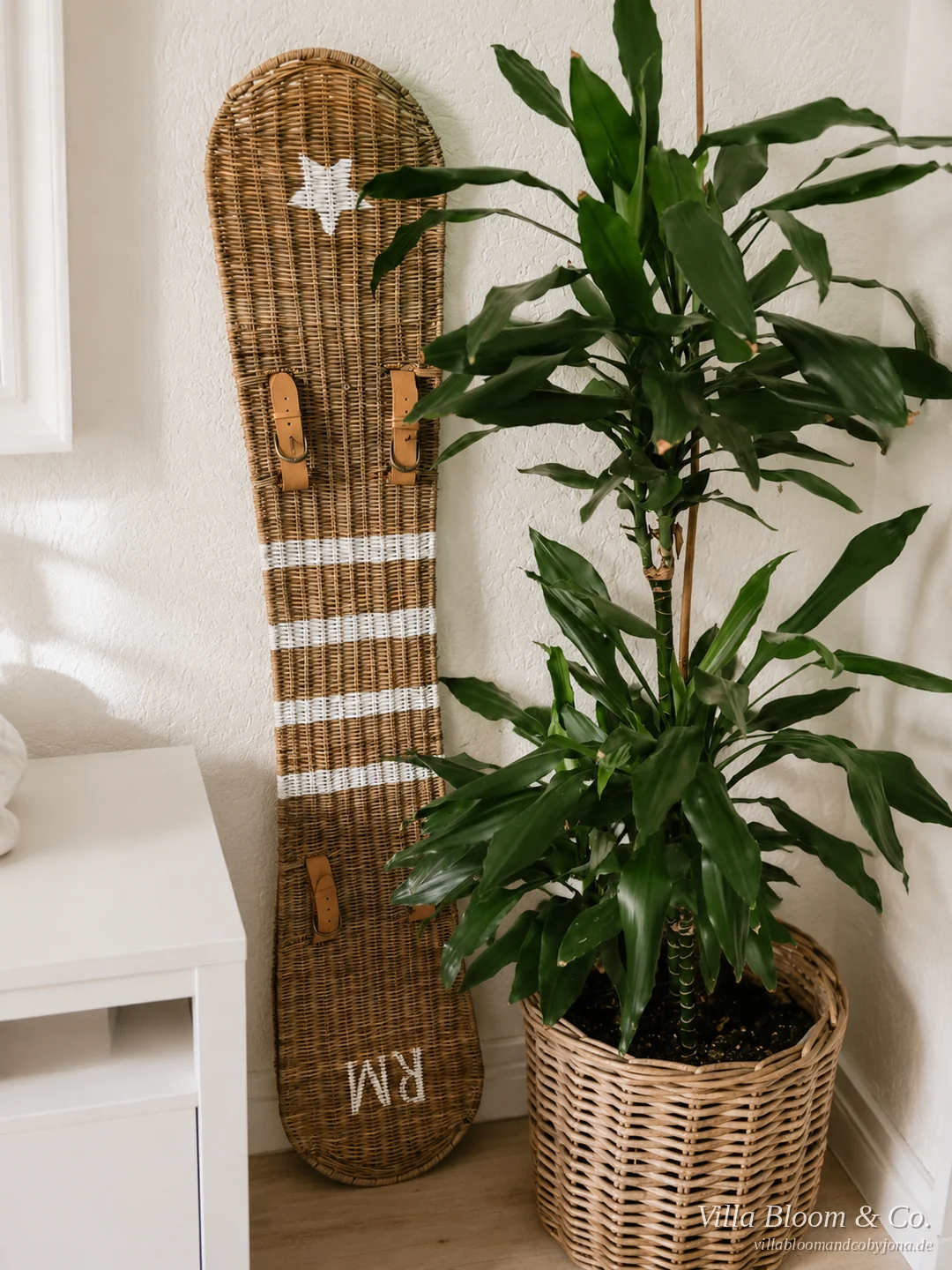 Snowboard aus Rattan mit Stern und RM-Schriftzug an der Wand neben einer Zimmerpflanze